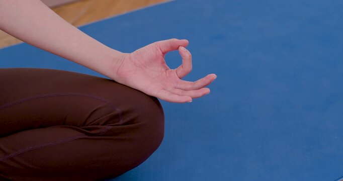 Close up of Asian woman forming meditation mudra while sitting on blue mat, practicing mindful breathing, calm concentration, yoga self care, stress relief routine, inner peace training session