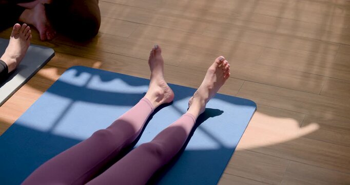 Asian yoga student performs slow motion foot flex and ankle mobility on mat during recovery practice, guided by trainer for joint comfort, circulation, flexibility, injury prevention indoors.