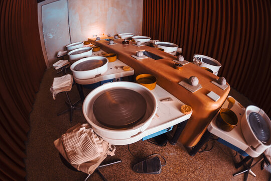 Empty ceramics classroom prepared for a hands-on lesson, featuring multiple electric pottery wheels, clay portions, water bowls, sponges, towels and stools; shot on a fish-eye lens
