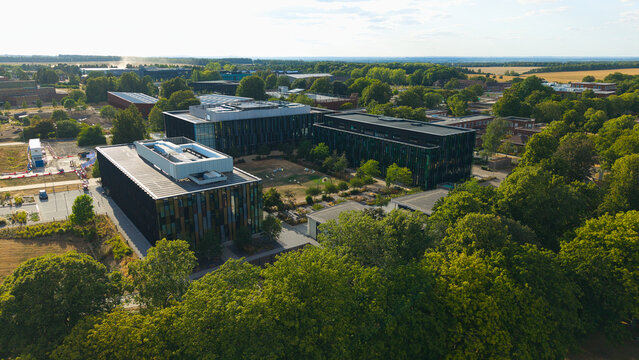 Aerial view of Resmed UK research campus featuring modern dark glass buildings surrounded by lush green trees and landscaped grounds in Didcot, England, United Kingdom.