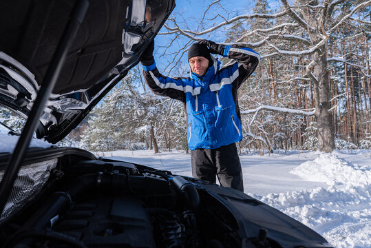 Driver inspect car engine after winter roadside breakdown