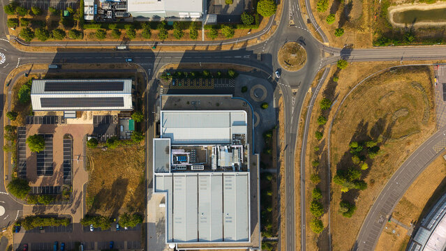 Aerial view of an innovation campus with rooftop HVAC ventilation and server cooling units, parking areas, and a roundabout in Harwell Oxford, England, United Kingdom.
