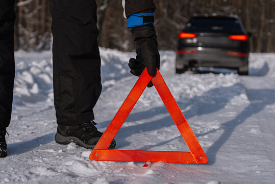 Driver placing warning triangle near car on snowy road
