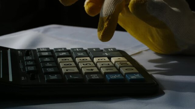 Close up construction worker hand wearing protective glove using calculator to estimate costs analyze budget manage project expenses on construction site office desk. Worker in glove using calculator