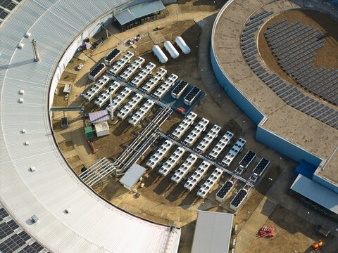 Aerial view of the Harwell Oxford campus featuring large circular buildings, rows of industrial HVAC cooling units, and rooftop solar panels in Harwell Oxford, England, United Kingdom.
