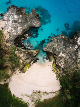Secluded sandy cove flanked by dramatic coral rock formations at Pantai Mandorak in Sumba, Indonesia