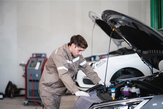 Experienced automotive mechanic inspecting the engine compartment of a passenger vehicle during routine maintenance and repair service inside a modern automotive workshop.