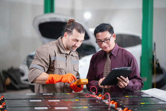 EV technician discussing battery inspection results with a customer while reviewing diagnostic information on a digital tablet in an automotive repair workshop.