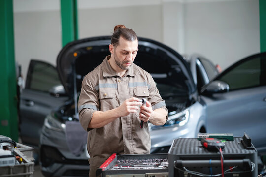Professional EV mechanic organizing and preparing repair tools before performing maintenance on an electric vehicle inside a modern automotive service center.