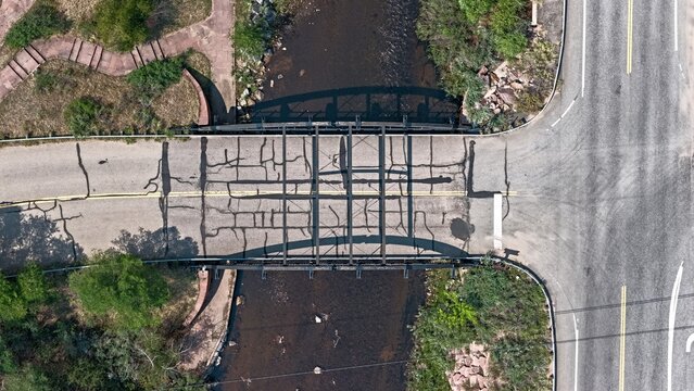 Aerial view of the Spring Gulch bridge spanning a creek, featuring weathered asphalt with visible cracks, steel girders, and surrounding greenery in Clear Creek County, Colorado, United States.