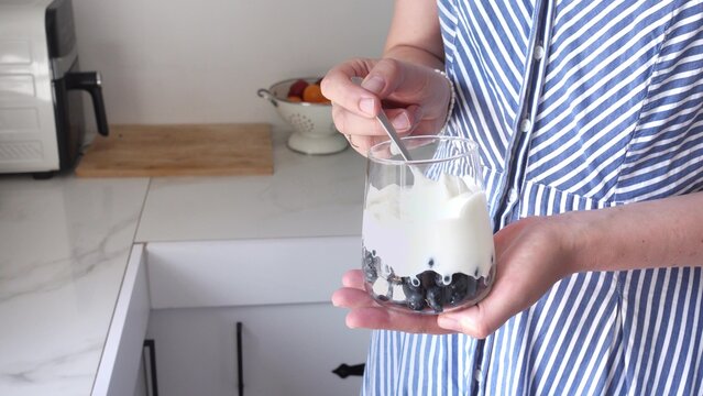 Woman stirs yogurt and berries in a glass with a spoon. Symbolizes probiotics, healthy eating, and the nutritional value of dairy products. Top view. Ideal for wellness, food, and lifestyle content