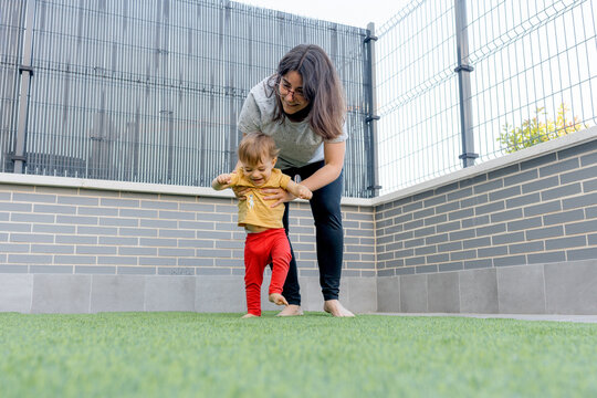 Mother help baby take first step on artificial grass