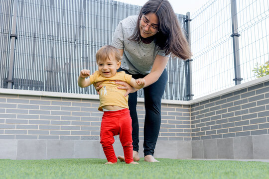 Mother help baby take first steps on artificial grass