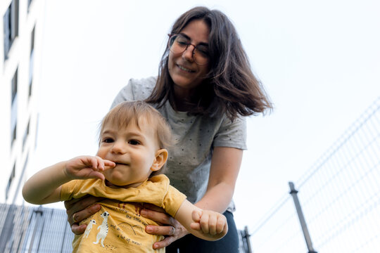 Mother holding toddler son outdoors near urban fence