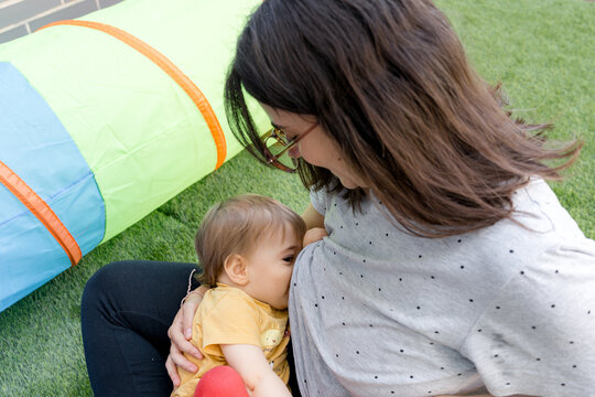 Mother breastfeeding baby beside play tent on artificial grass
