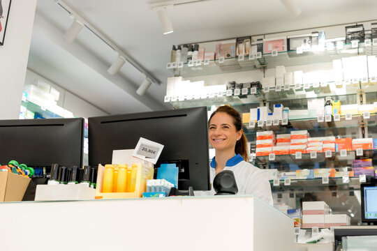 Smiling pharmacist at pharmacy counter with medicine shelves