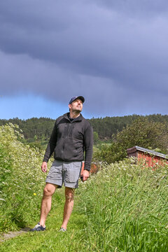 Man Standing in Tall Green Grass Looking Toward Sun in Norwegian Landscape