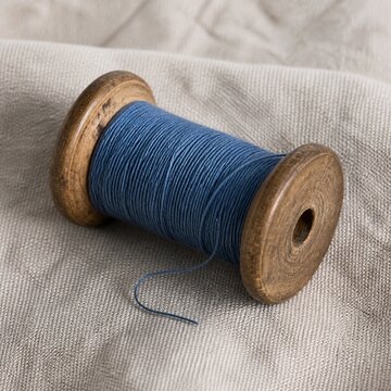Antique wooden bobbin with blue thread on textured linen fabric background