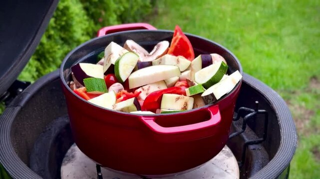A red clay pot filled with sliced vegetables, including zucchini (Cucurbita pepo), bell peppers (Capsicum annuum), mushrooms (Agaricus bisporus), and eggplant (Solanum melongena)