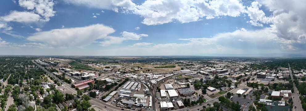 Aerial view of the city of Longmont featuring urban infrastructure, residential areas, and commercial buildings under a vast blue sky with scattered clouds in Longmont, Colorado, United States.