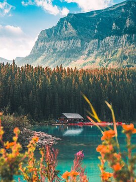 Scenic landscape of a rustic wooden boathouse and red canoes on a turquoise mountain lake surrounded by dense pine forest and majestic rocky peaks