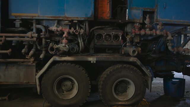 Industrial service truck midsection showing exposed pump housing, pipes, valves and dual rear wheels inside workshop bay with worn metal surfaces and heavy repair details