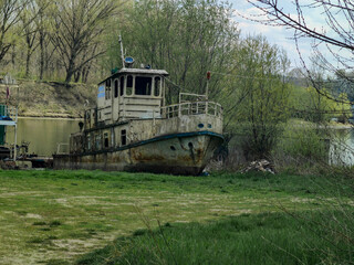 Old derelict boat on a peaceful riverside with lush spring vegetation. Ideal for themes of abandonment, maritime history, environmental change, travel, nostalgia and industrial decay. © Ana
