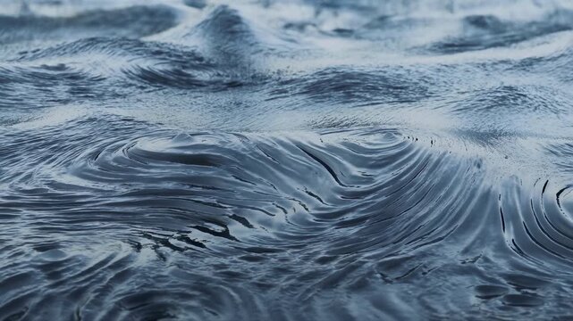 Dark blue water surface with layered ripples, curved wave folds, glossy reflections, swirling shapes, and calm abstract movement creating cool texture, depth, and atmospheric mood