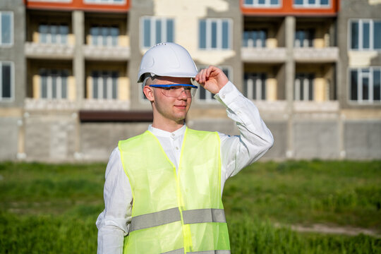 Construction worker adjusting helmet at new housing development site. Outdoor portrait of a foreman engaging in building inspection and safety measures