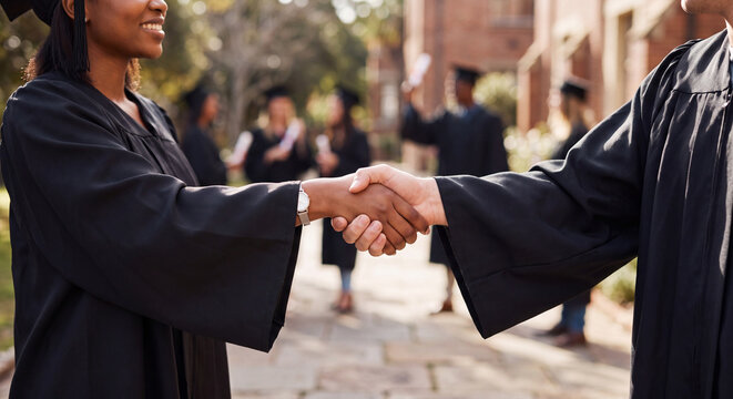 Two university graduates wearing black academic robes shake hands warmly during their commencement ceremony.