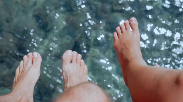 Couple Sitting on Pier and Swinging Feet Over Rippled Ocean Water