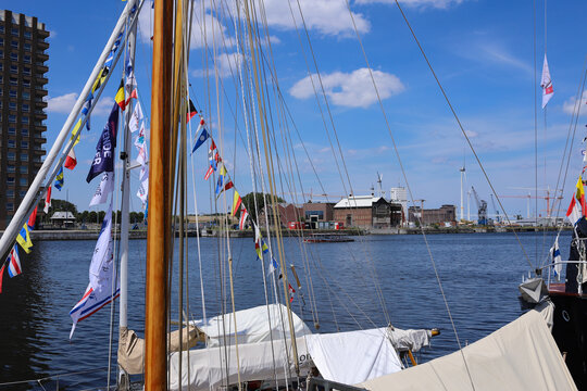 Horizontal view of sailboat mast decorated with colorful maritime flags in city port with harbor basin and blue sky background