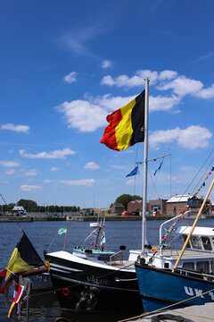 Belgian national flag waving on a boat mast at the city harbor under a blue cloudy sky