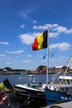 Belgian national flag waving on a ship mast in Antwerp harbor against a clear blue sky