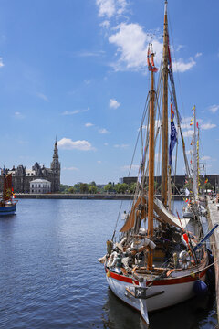 Classic wooden sailboat moored in Antwerp harbor with the historic Het Steen castle in the background on a sunny day