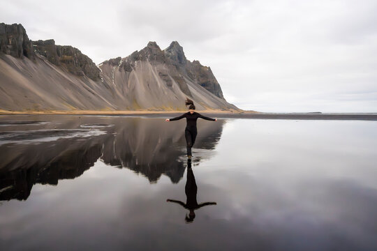 Woman on a reflective beach beneath Vestrahorn Mountain