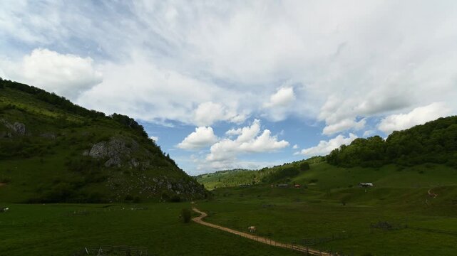Dynamic timelapse of dramatic clouds moving over the picturesque valley of Fundătura Ponorului, Romania. Rolling green hills, limestone cliffs, traditional rural landscape and a winding country road 