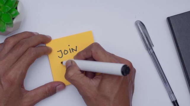 a man writing join now on orange sticky note