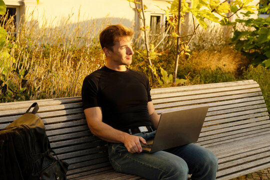 Young man use laptop on park bench at sunset