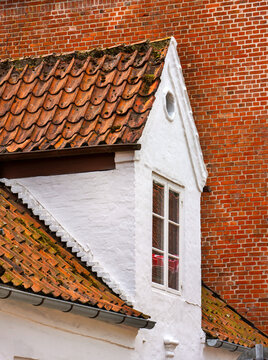 Traditional white dormer window on tiled roof with brick wall background