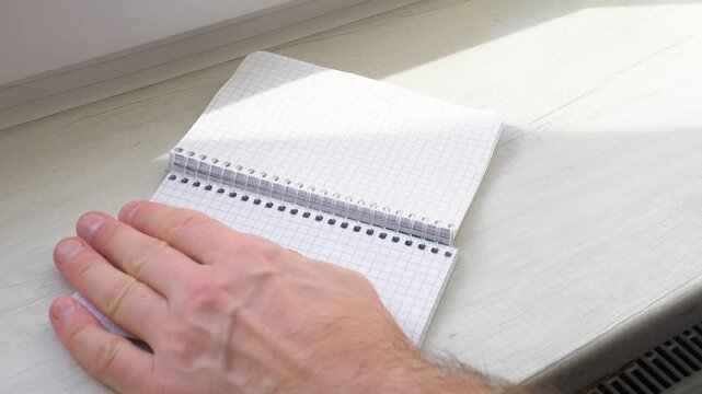 A man&rsquo;s hands tear a sheet of paper from a notepad. Tearing out sheets of paper from a notepad.