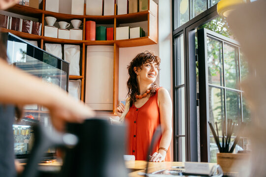 Stylish middle aged woman in orange dress smiling at counter in contemporary specialty cafe
