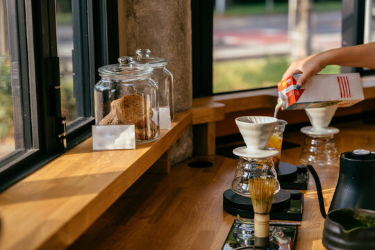 Professional barista pouring milk for iced matcha latte beside pour over setup in modern cafe