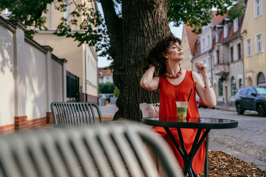 Relaxed middle aged woman in orange dress enjoying iced matcha at outdoor cafe table