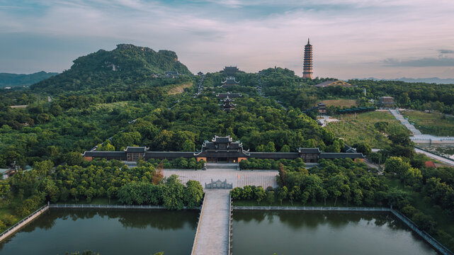 Aerial view of Bai Dinh Pagoda complex surrounded by lush greenery, stone walkways, and reflecting pools with mountains in the background in Tay Hoa Lu, Ninh Binh, Vietnam.