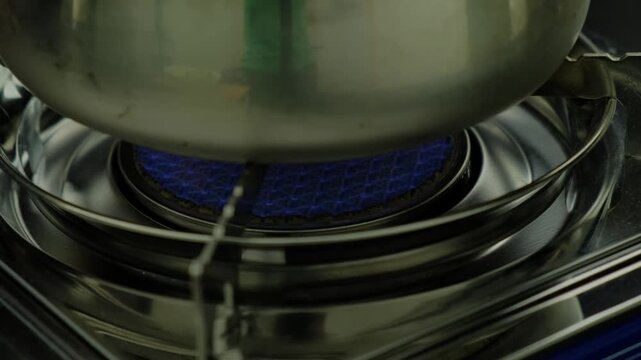 Close-up of a multi-tiered metal steamer with a blue grate cooking on a stove in a kitchen, person in green sleeves visible, Cooking location.