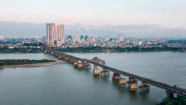 Aerial view of Long Bien Bridge spanning the Red River with the city skyline in the background at sunset, Hong Ha, Hanoi, Vietnam.