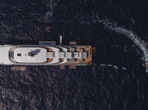 Aerial view of a large white superyacht anchored in the deep blue sea with a small tender and paddleboards nearby off the coast of Positano, Campania, Italy.
