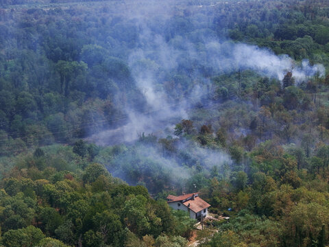 Aerial view of a fire in the Baraggia woodland with thick smoke rising above the trees near a residential house in Gattinara, Piedmont, Italy.