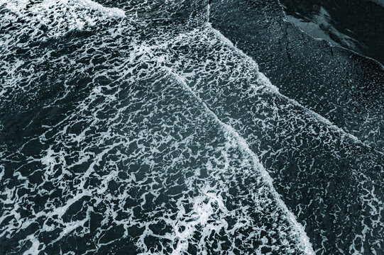 Aerial view of ocean waves crashing against the shoreline with white foam patterns on the dark blue water in Manzanillo, Limon Province, Costa Rica.